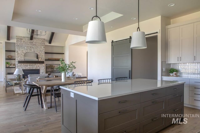 kitchen featuring hanging light fixtures, light wood-style flooring, a kitchen island, light countertops, and backsplash