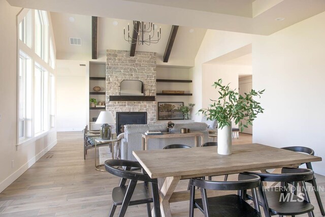 dining area with beam ceiling, light wood-type flooring, visible vents, a stone fireplace, and baseboards
