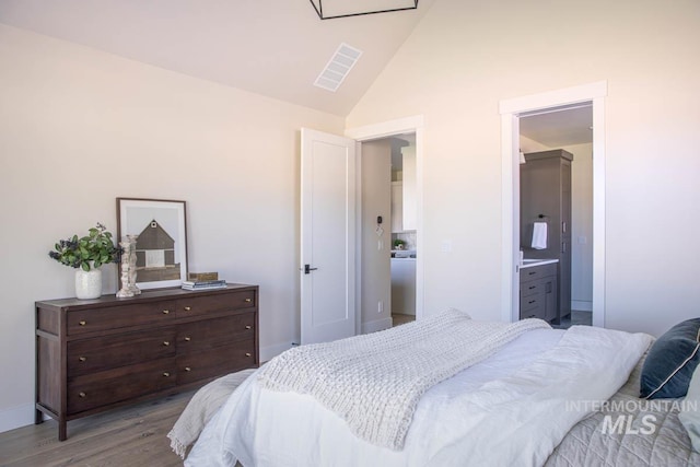 bedroom with lofted ceiling, visible vents, wood finished floors, and ensuite bathroom