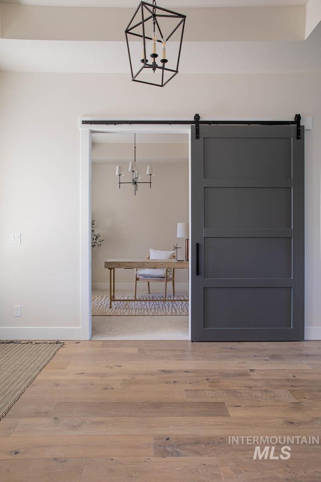 entryway featuring light wood finished floors, a notable chandelier, a barn door, and baseboards