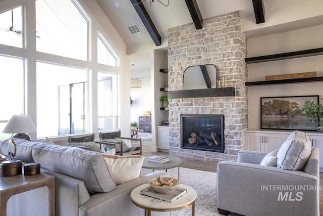 living room featuring wood finished floors, a fireplace, beam ceiling, visible vents, and a high ceiling