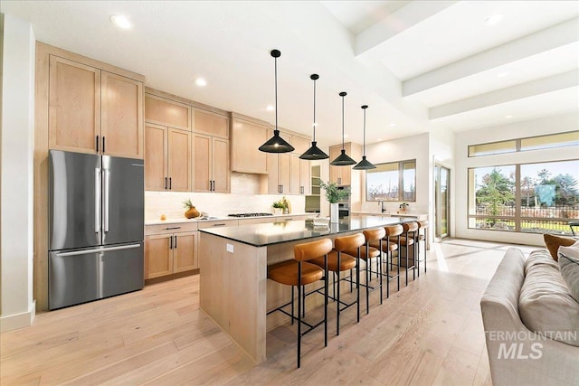 kitchen with a center island, hanging light fixtures, light brown cabinetry, light hardwood / wood-style floors, and stainless steel refrigerator