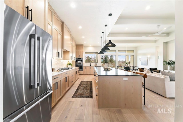 kitchen featuring decorative light fixtures, a kitchen island, light brown cabinetry, and appliances with stainless steel finishes