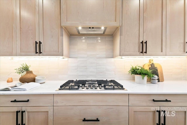 kitchen with decorative backsplash, light stone counters, light brown cabinetry, and stainless steel gas cooktop