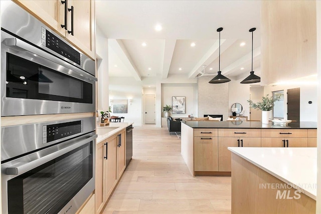 kitchen with light brown cabinetry, light wood-type flooring, double oven, beamed ceiling, and hanging light fixtures