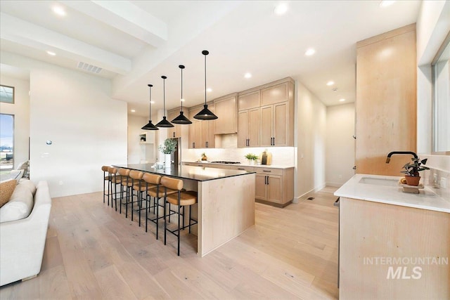 kitchen featuring sink, light brown cabinets, beam ceiling, pendant lighting, and light hardwood / wood-style floors