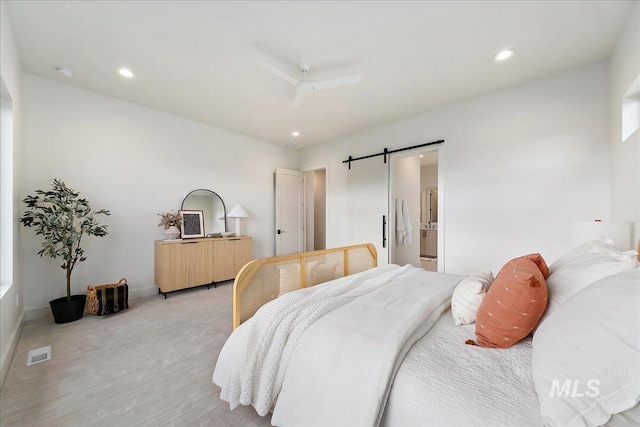 bedroom featuring a barn door, light colored carpet, ceiling fan, and connected bathroom