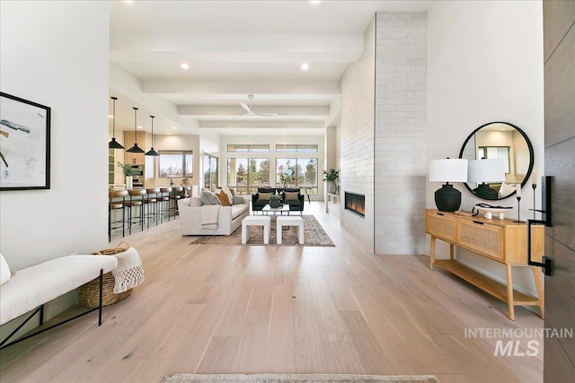 living room featuring beam ceiling, ceiling fan, a fireplace, and light hardwood / wood-style flooring