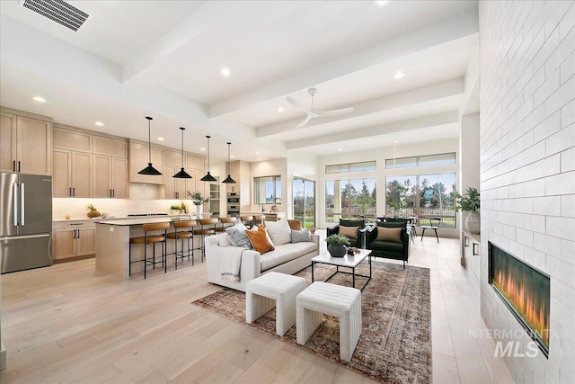 living room featuring ceiling fan, light hardwood / wood-style floors, beam ceiling, and a fireplace