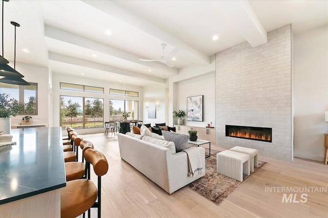 living room featuring beam ceiling, ceiling fan, a large fireplace, and light hardwood / wood-style flooring