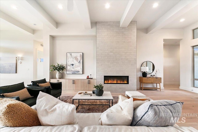 living room with beamed ceiling, light wood-type flooring, and a brick fireplace