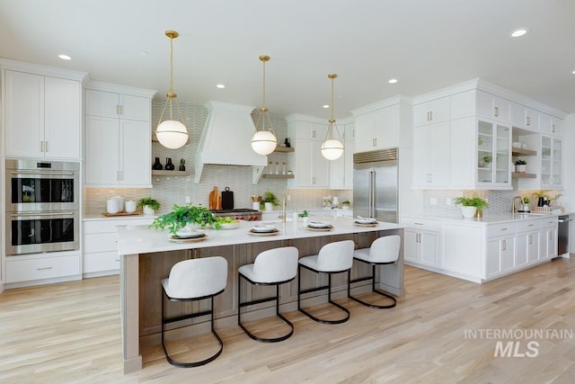 5935 E Marmount Ct, Boise, ID 83716 - kitchen featuring appliances with stainless steel finishes, open shelves, custom exhaust hood, light countertops, and a kitchen bar
