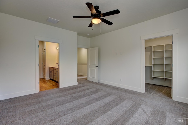 unfurnished bedroom with light carpet, ceiling fan, a spacious closet, and baseboards