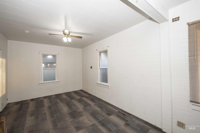 spare room featuring ceiling fan and brick wall