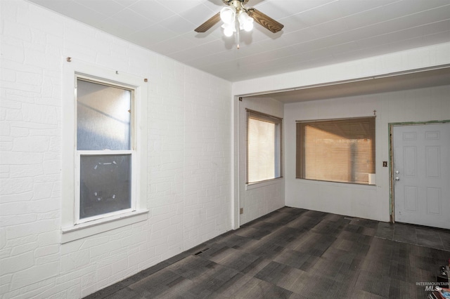 spare room featuring ceiling fan, dark wood-type flooring, and brick wall