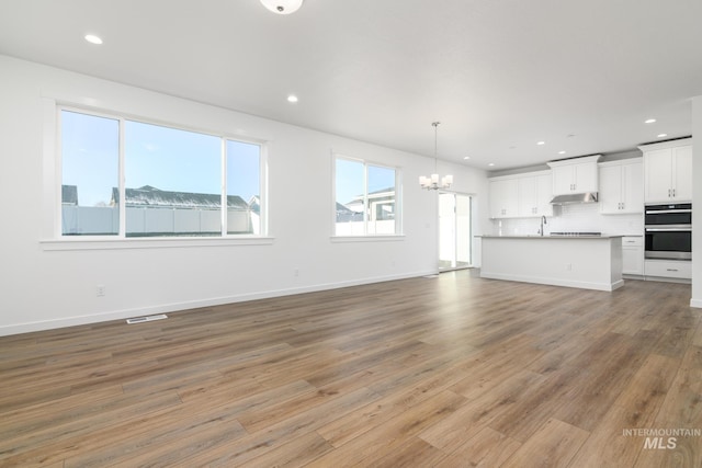 unfurnished living room featuring hardwood / wood-style floors, sink, and a chandelier