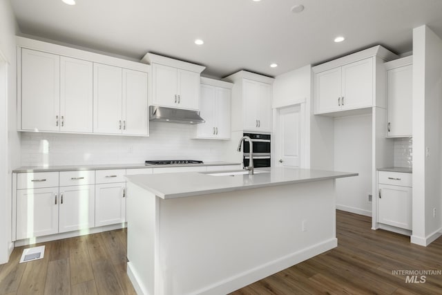 kitchen with dark hardwood / wood-style flooring, decorative backsplash, a center island with sink, and white cabinets