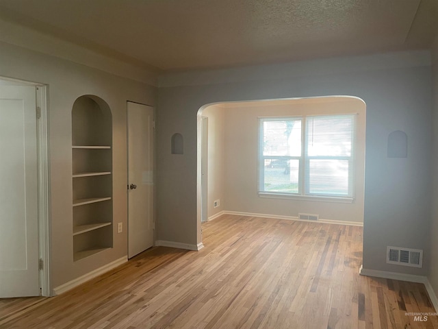 empty room featuring built in features, a textured ceiling, and light hardwood / wood-style flooring