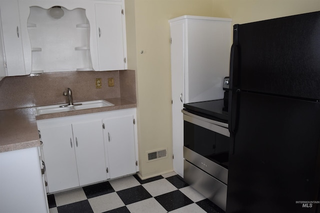 kitchen with backsplash, black refrigerator, sink, stainless steel range, and white cabinets