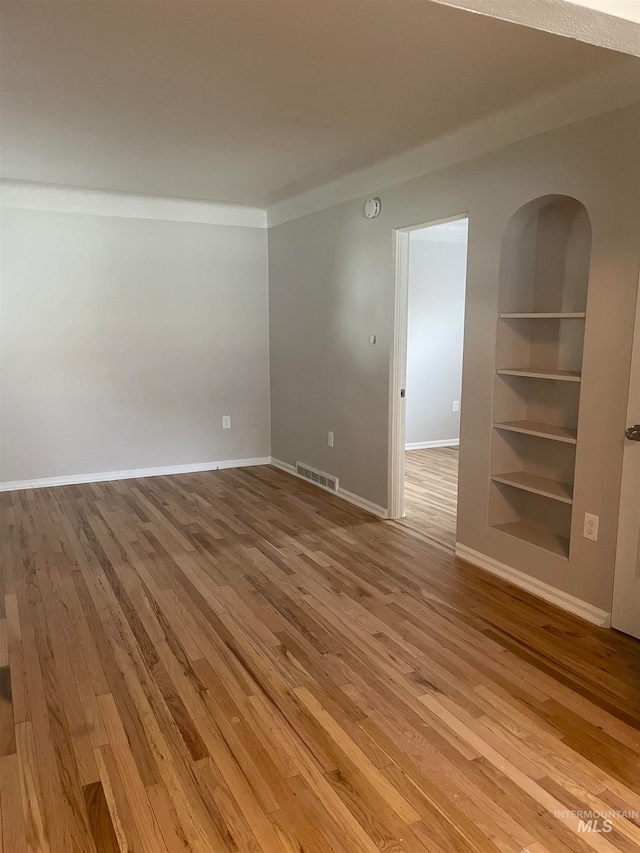 spare room with built in shelves and wood-type flooring