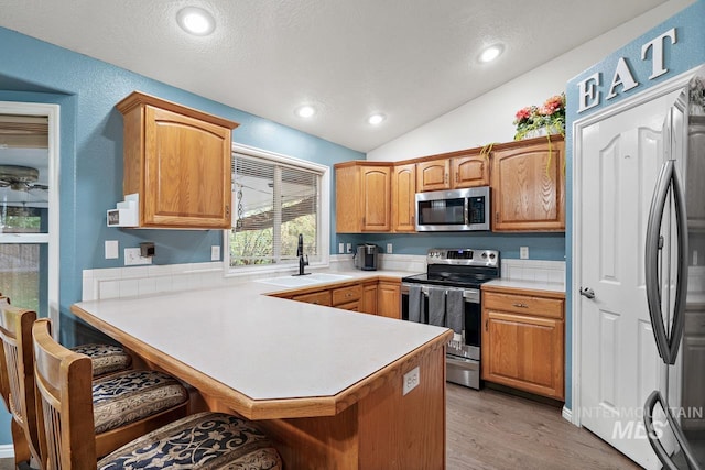 kitchen with light wood-type flooring, sink, appliances with stainless steel finishes, lofted ceiling, and kitchen peninsula