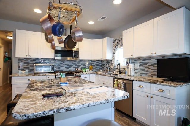kitchen with visible vents, a sink, appliances with stainless steel finishes, dark wood-style floors, and light stone counters