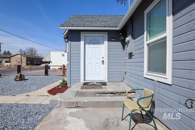 view of exterior entry featuring roof with shingles and fence