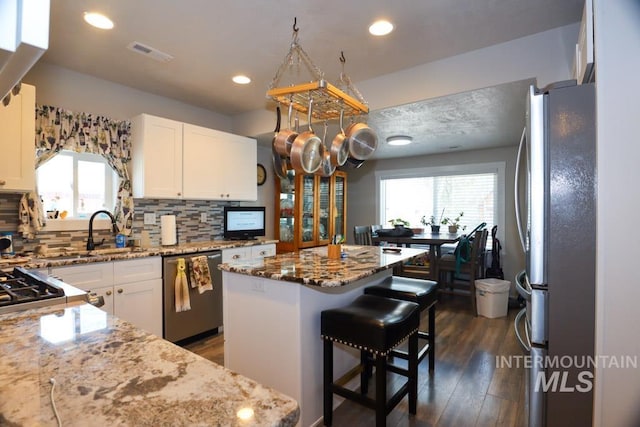 kitchen with tasteful backsplash, visible vents, a center island, light stone counters, and stainless steel appliances