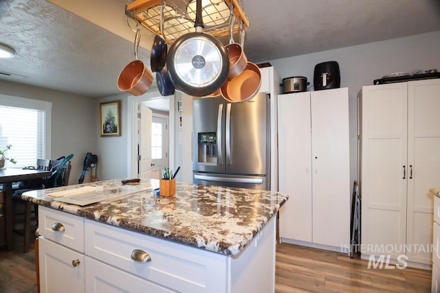 kitchen featuring stainless steel fridge, a center island, white cabinetry, light stone countertops, and wood finished floors