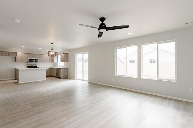 unfurnished living room featuring ceiling fan, sink, and light wood-type flooring