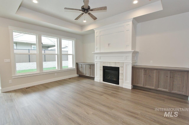 unfurnished living room featuring a glass covered fireplace, a raised ceiling, and light wood finished floors