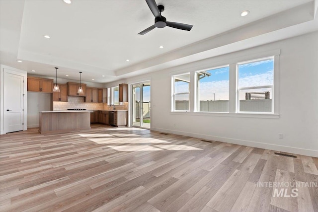 unfurnished living room featuring ceiling fan, sink, a tray ceiling, and light hardwood / wood-style floors