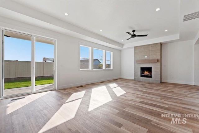 unfurnished living room featuring ceiling fan, a raised ceiling, a tile fireplace, and light wood-type flooring