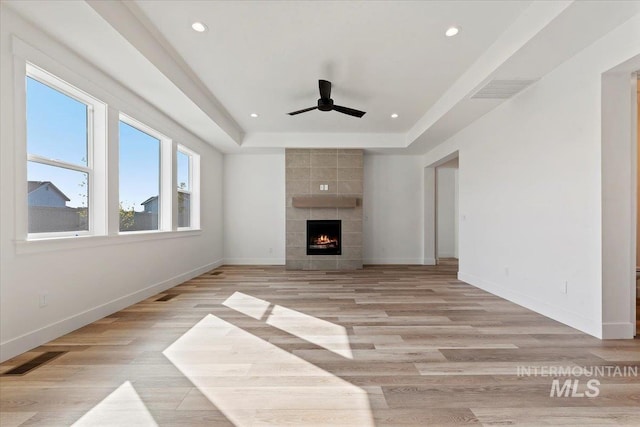 unfurnished living room featuring a tiled fireplace, light hardwood / wood-style flooring, a raised ceiling, and ceiling fan