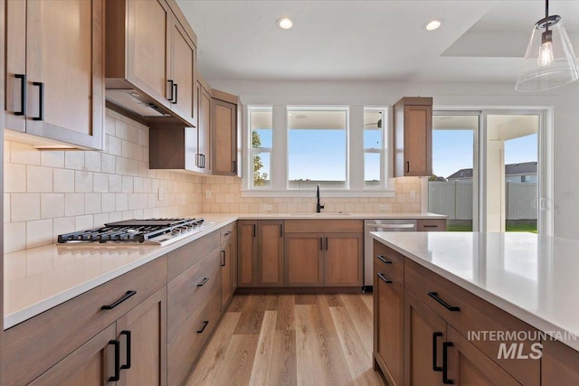 kitchen featuring appliances with stainless steel finishes, decorative light fixtures, sink, backsplash, and light hardwood / wood-style flooring