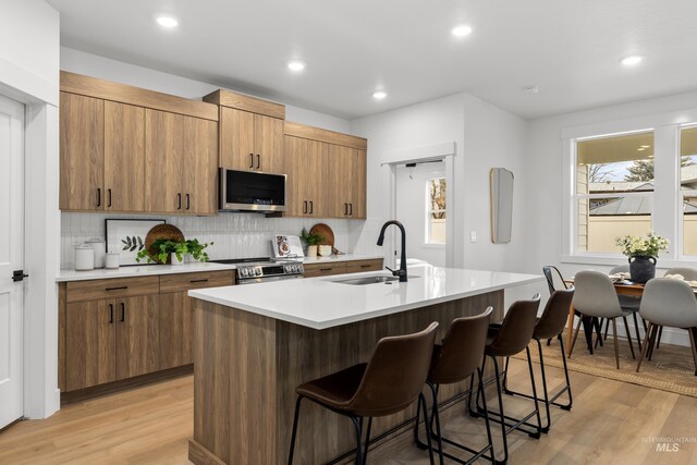 kitchen featuring sink, stainless steel appliances, an island with sink, and light hardwood / wood-style flooring