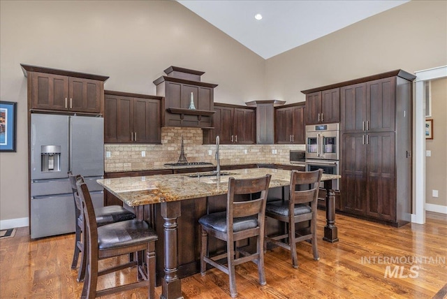 kitchen with dark brown cabinets, light stone countertops, high vaulted ceiling, stainless steel appliances, and decorative backsplash