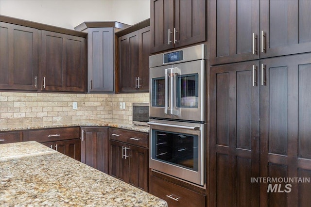 kitchen with double oven, light stone counters, dark brown cabinets, and tasteful backsplash