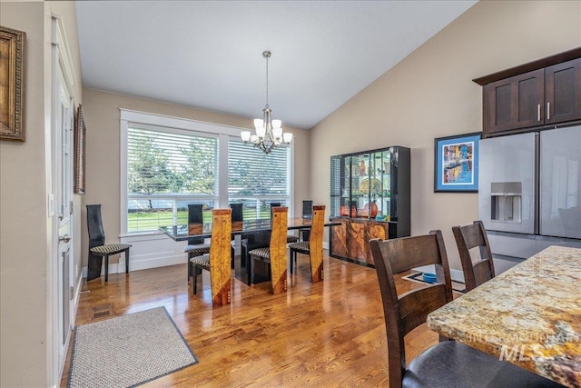 dining area with baseboards, vaulted ceiling, an inviting chandelier, and light wood-style floors