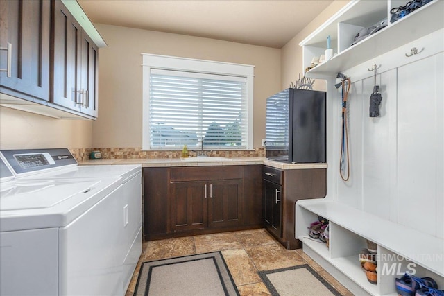 clothes washing area with cabinet space, stone finish flooring, a sink, and washing machine and clothes dryer