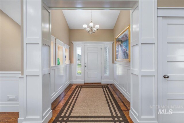 foyer featuring dark wood-style flooring, a decorative wall, and a notable chandelier