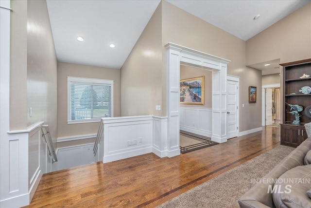 corridor featuring an upstairs landing, wood finished floors, a wainscoted wall, lofted ceiling, and a decorative wall