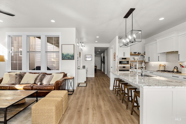 kitchen with light stone counters, pendant lighting, light wood-type flooring, white cabinets, and appliances with stainless steel finishes