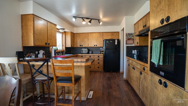 kitchen featuring under cabinet range hood, a peninsula, brown cabinets, decorative backsplash, and black appliances