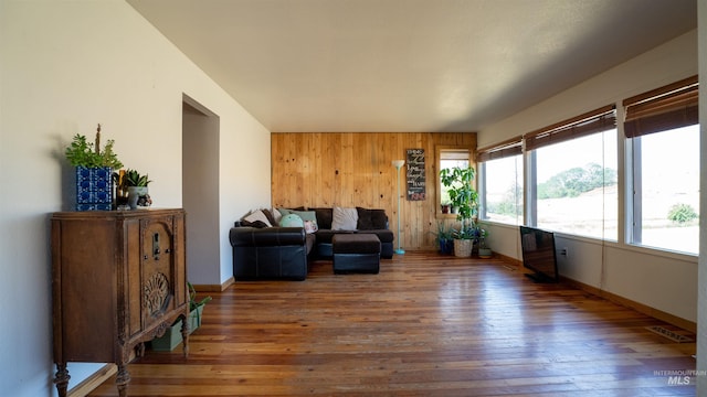 living room with wood-type flooring, wooden walls, and baseboards