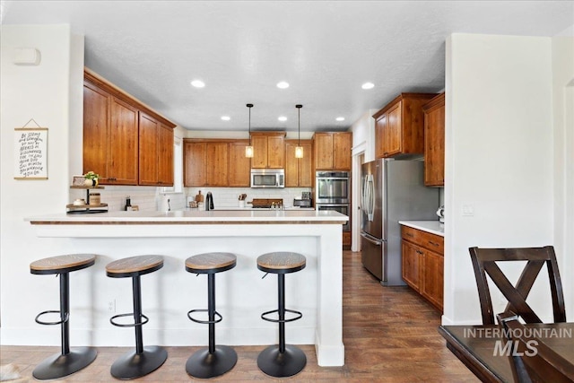 1041 White Horse Ridge Dr, Middleton, ID 83644 - kitchen with appliances with stainless steel finishes, a peninsula, brown cabinetry, dark wood-style floors, and a breakfast bar