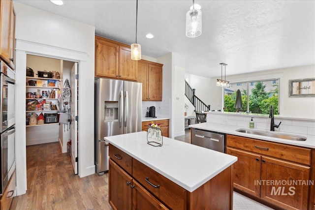 1041 White Horse Ridge Dr, Middleton, ID 83644 - kitchen featuring stainless steel appliances, a sink, brown cabinetry, wood finished floors, and decorative backsplash