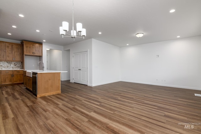 kitchen with dark wood-type flooring, hanging light fixtures, black dishwasher, tasteful backsplash, and a center island with sink