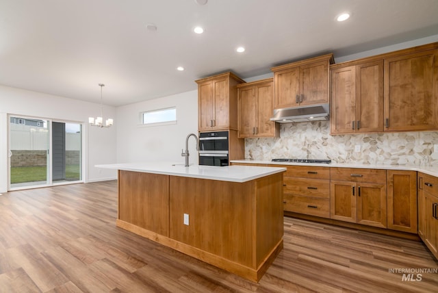 kitchen with hardwood / wood-style floors, decorative light fixtures, stainless steel gas stovetop, and a center island with sink