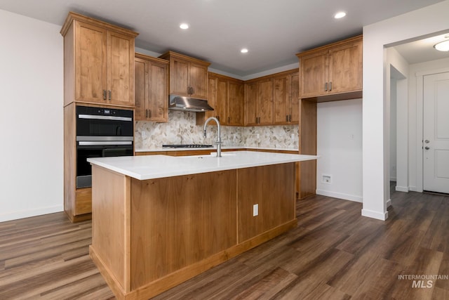 kitchen with decorative backsplash, black double oven, dark hardwood / wood-style floors, and a center island with sink